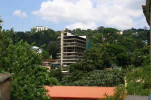 a tall white building on a hill with trees at City Nest Inn in Kandy