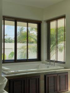 a bathroom with a tub and three windows at Brown Cotton Villa Khanom in Khanom