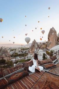 a woman sitting on a roof watching hot air balloons at Anatolian Houses Cave Hotel & SPA in Goreme