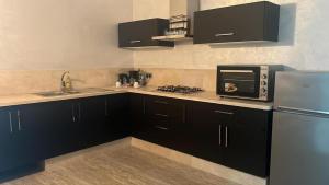 a kitchen with black cabinets and a microwave and a refrigerator at DAR RAS EL MA PLAGE in Ras El Ma