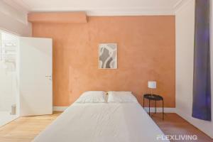 une chambre avec un lit blanc et un mur orange dans l'établissement Flexliving - room - Neuilly-sur-Seine, à Neuilly-sur-Seine
