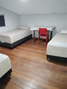 a room with two beds and a table and a red chair at Pousada do Bosque-Hostel in Rio Branco