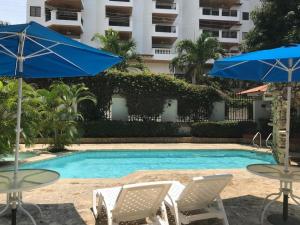 a swimming pool with two tables and blue umbrellas at Apartment Bello Horizonte in Santa Marta