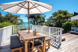 une table en bois avec un parasol sur une terrasse dans l'établissement Picnic Bay Vista - Be My Guest Waiheke, à Putaki Bay