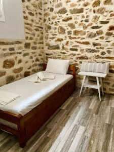 a bed and a chair in a room with a stone wall at Porto Levante Anemos in Ermoupoli