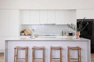 a kitchen with white cabinets and bar stools at Free night! Pay for 2 stay for 3 in Narrawallee