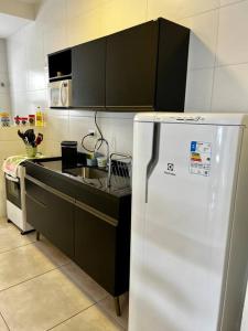 a kitchen with a white refrigerator and black cabinets at Apê Jardins 212 - Piscina, Churrasqueira, 2 Quartos a 600m da Orla Central in Ubatuba