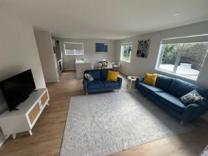 a living room with two blue couches and a flat screen tv at Bach At 45 in Ahipara +16 photos