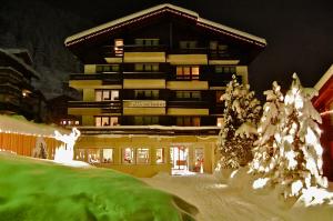 un grand bâtiment avec des arbres enneigés devant lui dans l'établissement Hotel Garni Jägerhof, à Saas-Fee