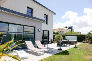 a patio with white chairs and tables and an umbrella at Villa Enora Bretagne Piscine Intérieure Partagée Jacuzzi privatif 100m Plage in Sibiril