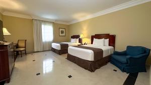 um quarto de hotel com duas camas e uma cadeira em Hotel El Prado em Barranquilla