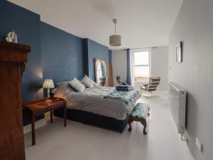 a bedroom with blue walls and a bed and a table at Tonnau Yr Oleu or Waves of Light in Barmouth