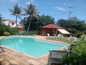 a swimming pool with chairs and a gazebo at Vila Hibisco Pousada Saquarema in Saquarema