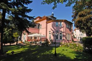 uma casa cor-de-rosa com um relvado à frente. em Parkhotel Güldene Berge em Weißenfels