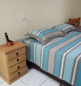 ein Schlafzimmer mit einem Bett und einem Nachttisch mit einer gestreiften Decke in der Unterkunft Chalé Vitória 1- Rancho dos 7 in Arapeí