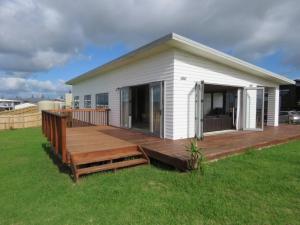 a house with a wooden deck in the grass at Cleggs Batch in Karikari Peninsula