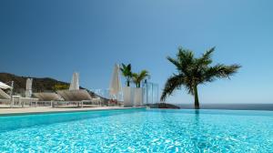 a swimming pool with chairs and a palm tree at Grand Horizon Luxury Boutique Apartments in Puerto Rico de Gran Canaria