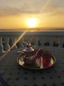 a tea set on a plate on a balcony with the sunset at Panoramic Ocean View Escape - Luxury Duplex in Villa in El Jadida