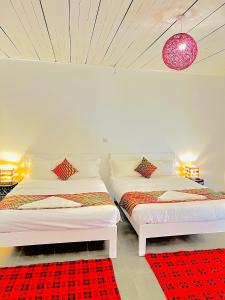 two beds in a white room with a red rug at KaChai Hotel Fort Portal in Kyarusozi
