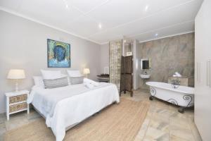 a bedroom with a large white bed and a bath tub at Land's Edge Eco Friendly Cottages and Apartments in Struisbaai