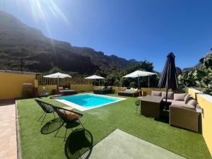 a backyard with a pool and chairs and an umbrella at SUNNY CARMELITO DELUXE in Mogán