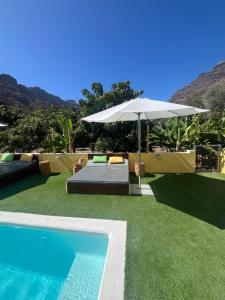 a swimming pool with an umbrella and a bed at SUNNY CARMELITO DELUXE in Mogán