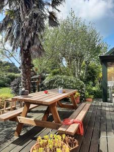 a wooden picnic table on a deck with a palm tree at La Maison Rose - avec grand jardin clos à 300m de la mer in Hauteville-sur-Mer
