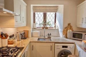 a kitchen with white cabinets and a sink and a window at Danes Cottage - Luxury Peak District Retreat in Chapel en le Frith