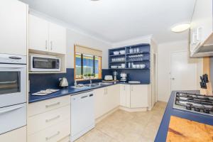 a kitchen with white cabinets and blue walls at The Observation Deck by Experience Jervis Bay in Sanctuary Point