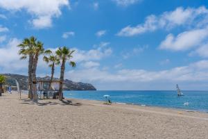 a beach with palm trees and a sailboat in the ocean at Apto Mediterraneo 7 La Herradura in La Herradura