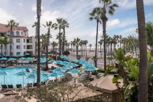 einen Pool mit blauen Sonnenschirmen, Stühlen und Palmen in der Unterkunft Hyatt Regency Huntington Beach Resort and Spa in Huntington Beach