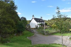 a white house on a hill with a gravel driveway at Ardmore Shepherd's Hut in Lochinver