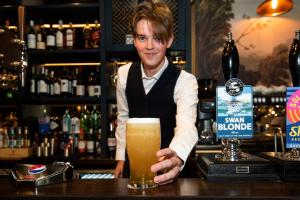 a man standing behind a bar holding a glass of beer at The Swallow Falls Inn - The Inn Collection Group in Betws-y-coed