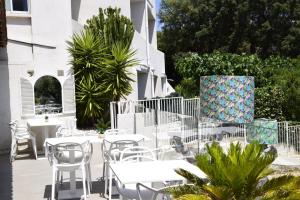 a patio with white tables and chairs and plants at Hotel La Voile in Bormes-les-Mimosas