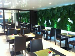 a restaurant with tables and chairs and a green wall at Hôtel du Val de Seine in Mantes-la-Jolie