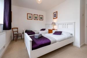 two beds in a white bedroom with purple sheets at Splendid House Great Location to WAVE Surf & South West Water Park - Super Garden By StayStaycations in Bristol