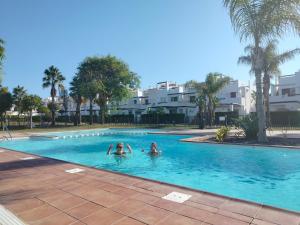 twee mensen zwemmen in een zwembad met palmbomen bij Condado de Alhama Golf resort - Villa Alba in Alhama de Murcia