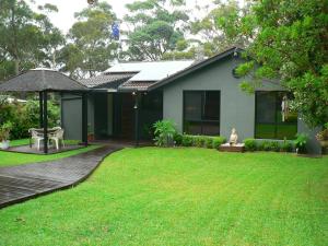 a house with a green yard with a wooden deck at Waterfront Jervis Bay Escape Cooinda in Sanctuary Point