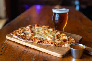 a pizza on a wooden cutting board next to a glass of beer at Atlantic Pub & Hotel in Glen Robertson