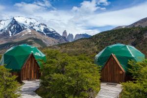 twee houten hutten met groene parasols in de bergen bij Ecocamp Patagonia in Torres del Paine