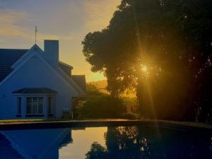 a house with the sun setting behind a tree at Menuha Landgoed in Gqeberha