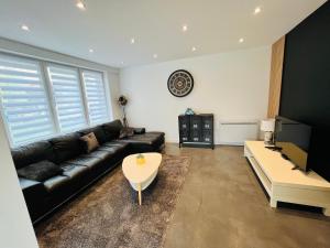 ein Wohnzimmer mit einer schwarzen Ledercouch und einem Tisch in der Unterkunft Maison contemporaine proche de Lille in Saint-André