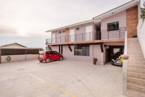 une voiture rouge garée dans un parking en face d'une maison dans l'établissement Studio 3 - Linda vista beira-mar, à Florianópolis