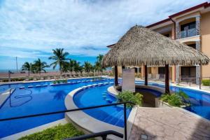 a resort with a large swimming pool with a straw umbrella at Jaco Beachfront Oasis Newly renovated dream condo in Jacó