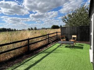 um banco e duas cadeiras sentados num relvado ao lado de uma cerca em Lavender Lodge - Pool and Hot Tub with sunset views over open fields em Wymondham