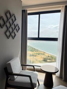 a living room with a chair and a table and a large window at APEC MANDALA CHAMBAY Thanh La Home in Phan Thiet