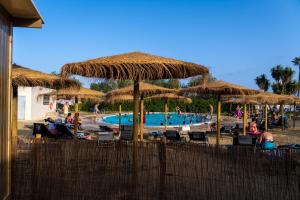 a pool with straw umbrellas and people sitting around it at TAIGA Almeria Playa in Palomares