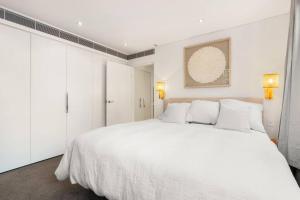 ein weißes Schlafzimmer mit einem großen weißen Bett mit weißen Kissen in der Unterkunft Vogue charm w light, aspect, AC in Sydney
