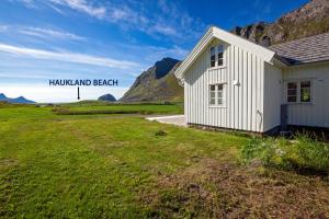 a small white building in a field next to a mountain at The Haukland House, Between Peaks & Sea in Leknes