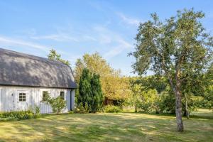 an old white barn with a tree in the yard at Woodfield Cottage Skåne in Vollsjö